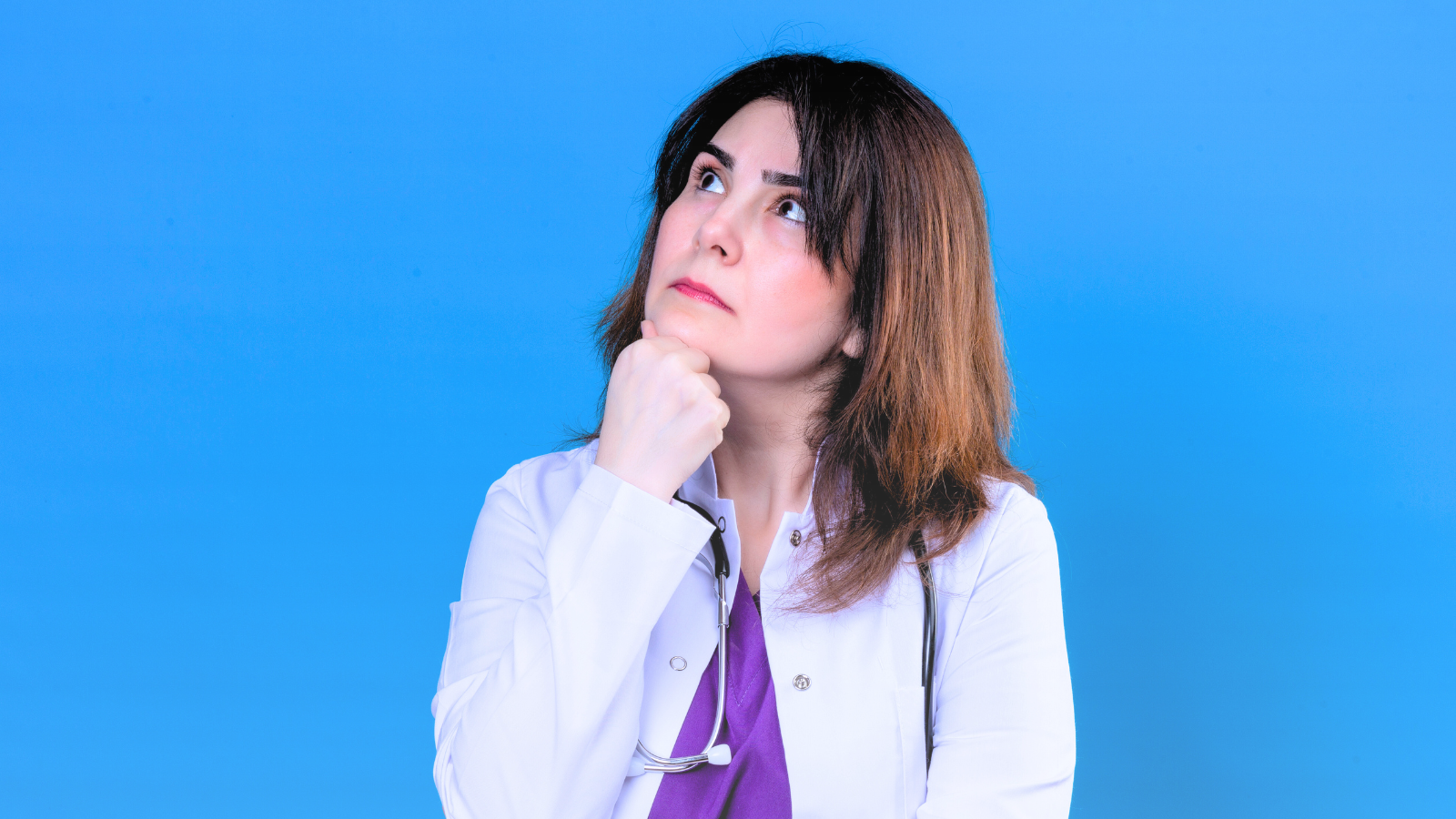 A woman in a white coat appears deep in thought, with a contemplative expression on her face.