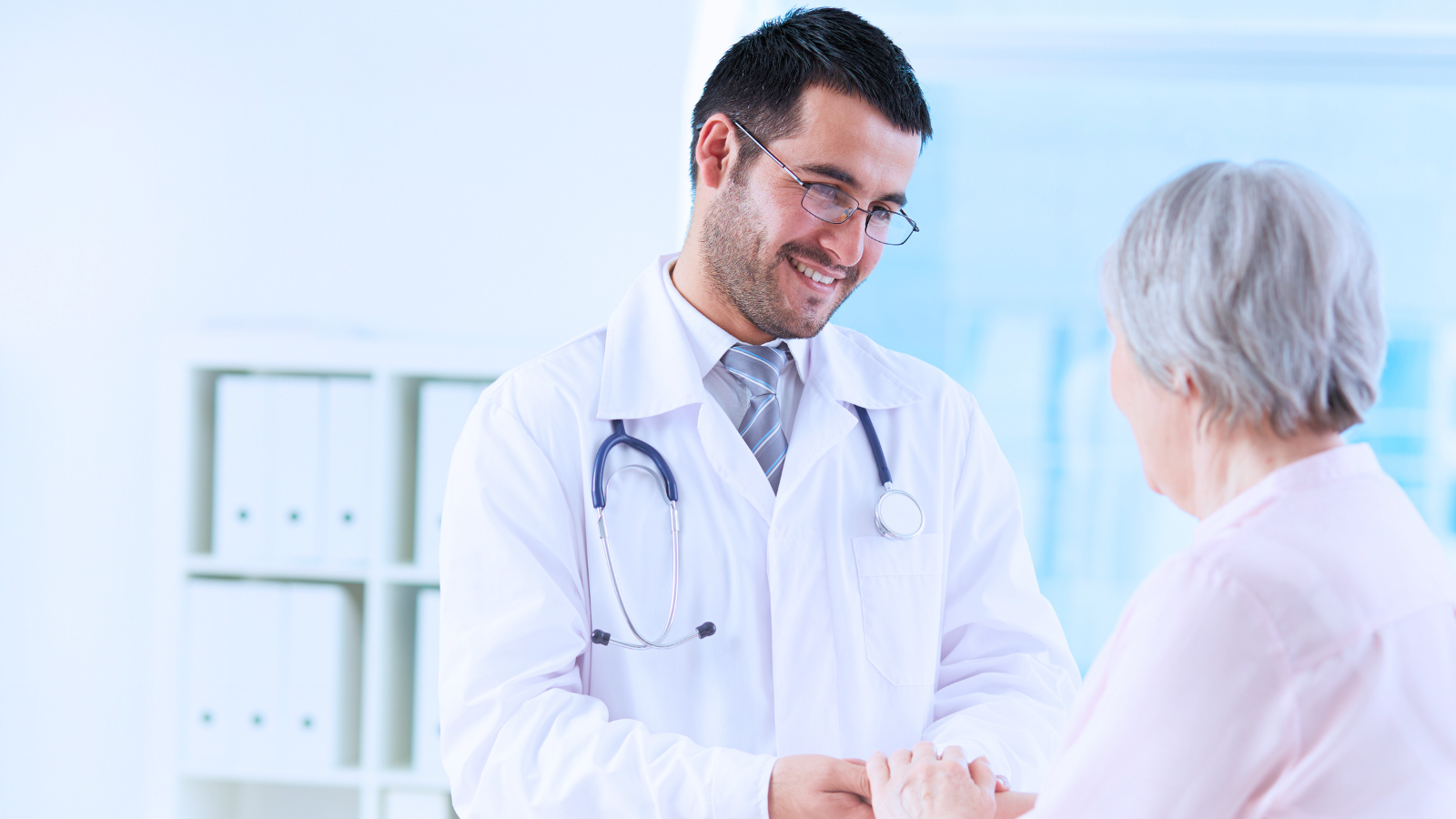 A male doctor shakes hands with an elderly woman, symbolizing care and trust in a medical setting.