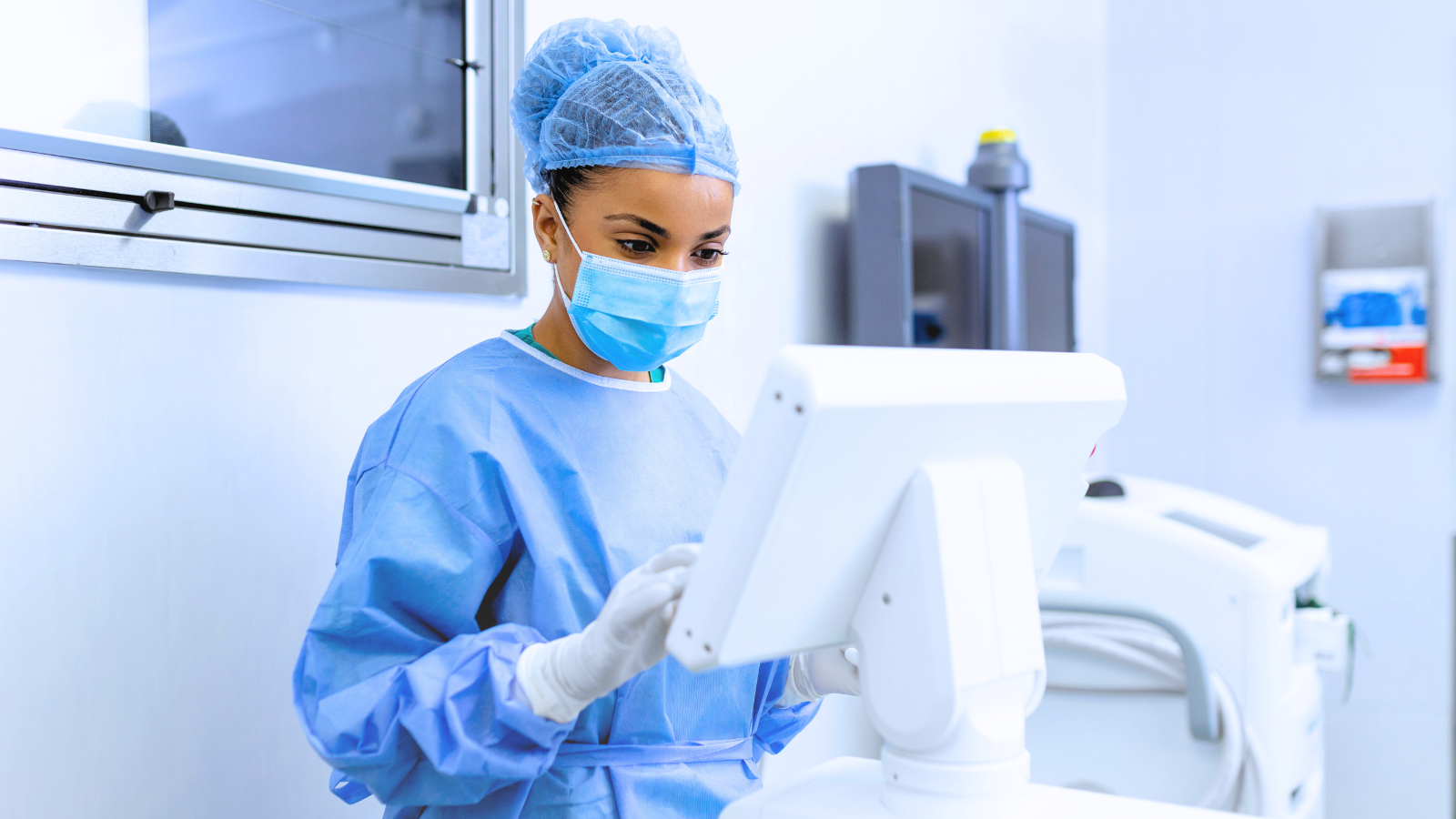 A woman in a surgical gown is focused on using a computer in a clinical setting.