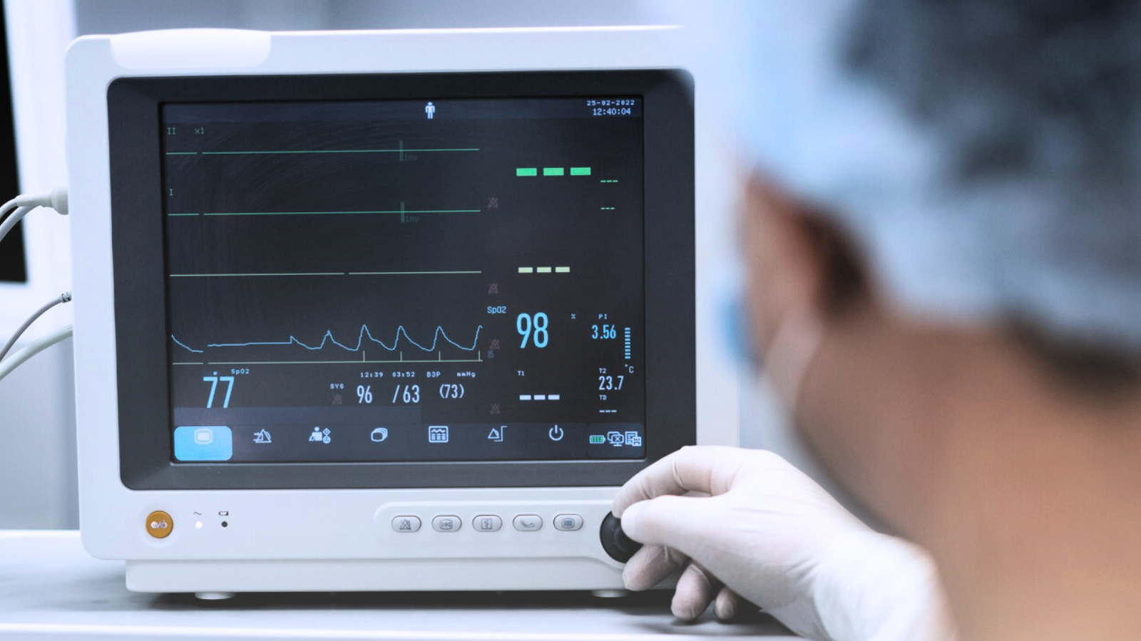 A person in a hospital room interacting with an electronic monitor, surrounded by medical equipment and soft lighting.