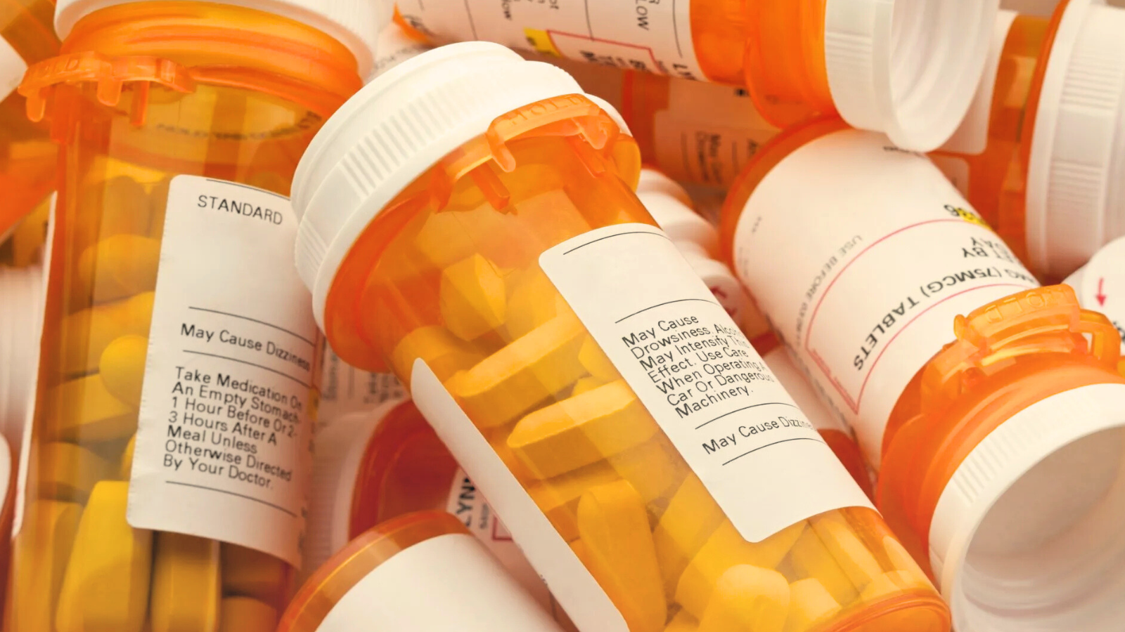 Prescription bottles stacked together, showcasing various labels and colors, indicating a collection of medications.