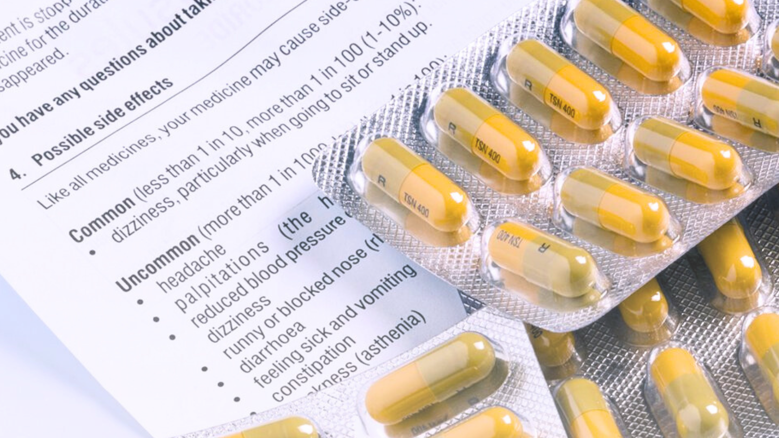 A pack of pills rests on a wooden table, their contents visible through the transparent packaging. Next to it lies a document with medical instructions for using the medications.